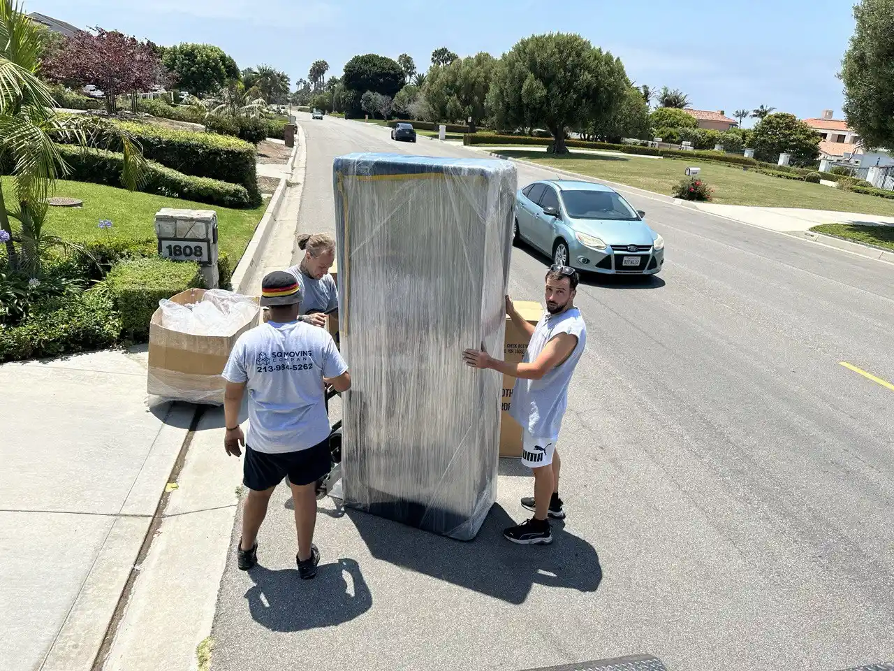 Affordable moving company in Encino – SQ Moving Company team wrapping and transporting a large household item on a residential street