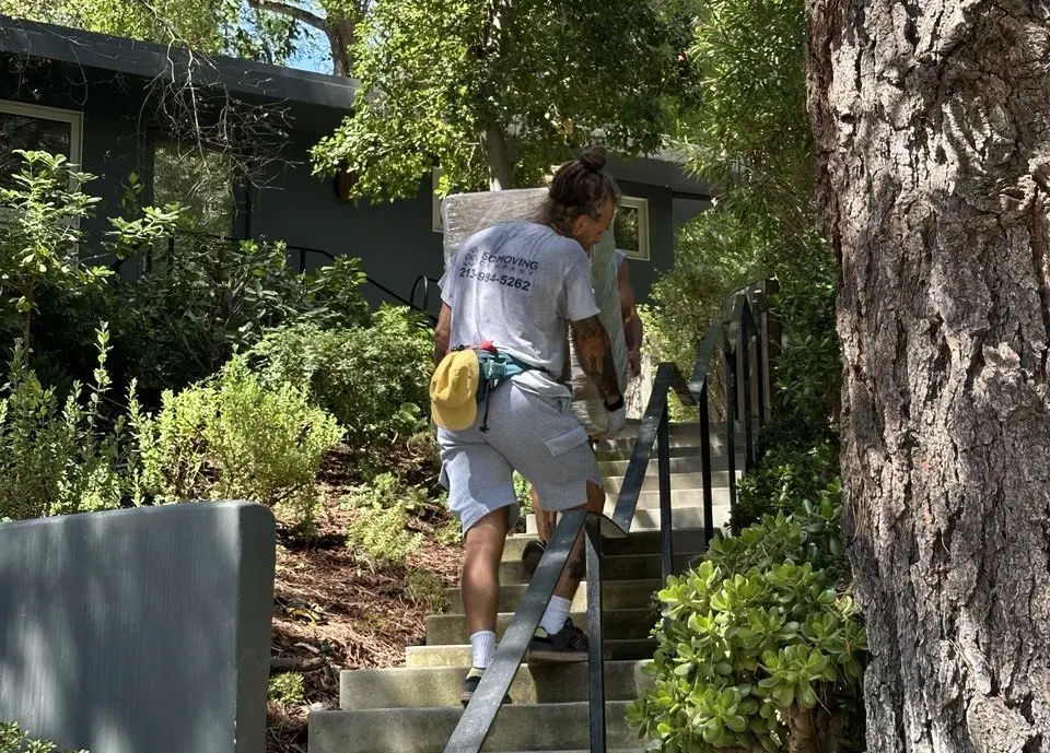 Movers in Sierra Madre carrying a heavy cabinet by hand on top of a hillside home