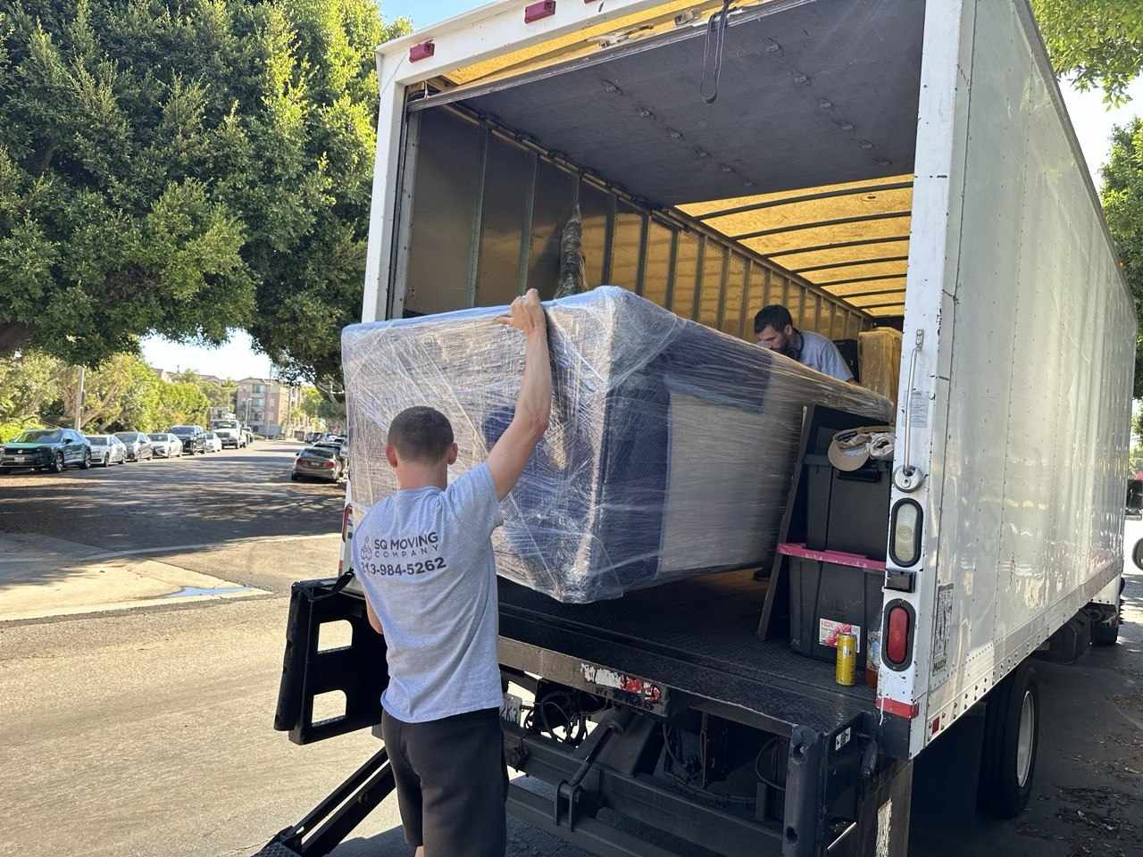 Professional SQ Moving Company movers in Palms, CA safely loading a fully wrapped couch into the truck during a local residential move.