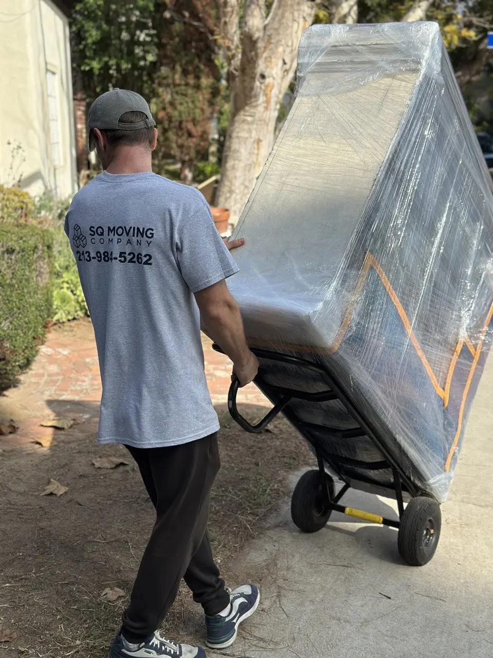 Redondo Beach moving company crew member transporting a fully wrapped dresser on a dolly during a residential move.