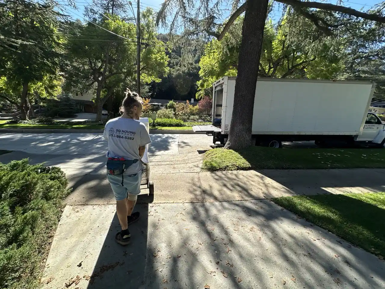 Professional movers in Sierra Madre handling a residential move—team member walking down a driveway carrying moving equipment with a truck parked on a tree-lined street
