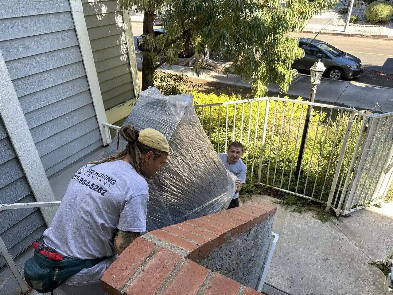 Downtown Los Angeles movers carefully carrying a large wrapped dresser up exterior stairs at a residential home