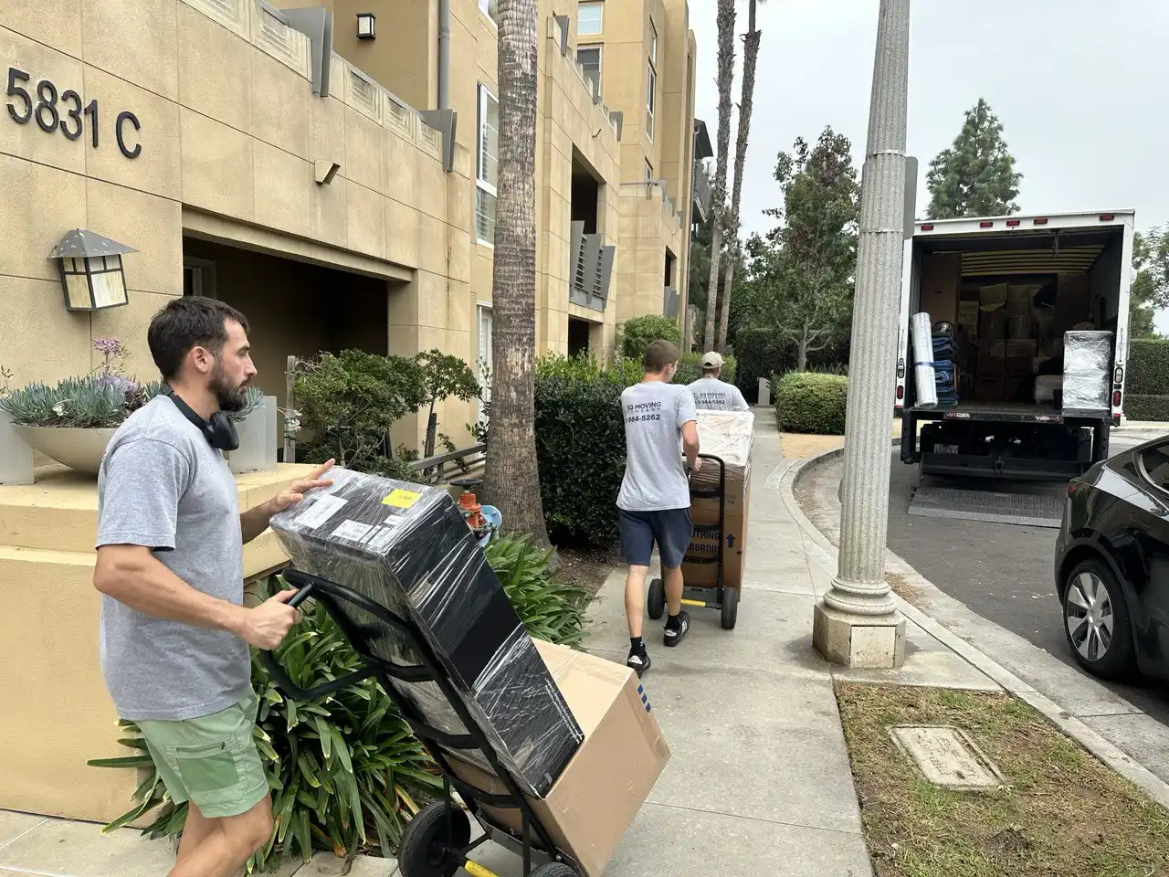SQ Moving Company crew using dollies to move packed boxes from an apartment building into a box truck during a residential move in Arcadia, CA