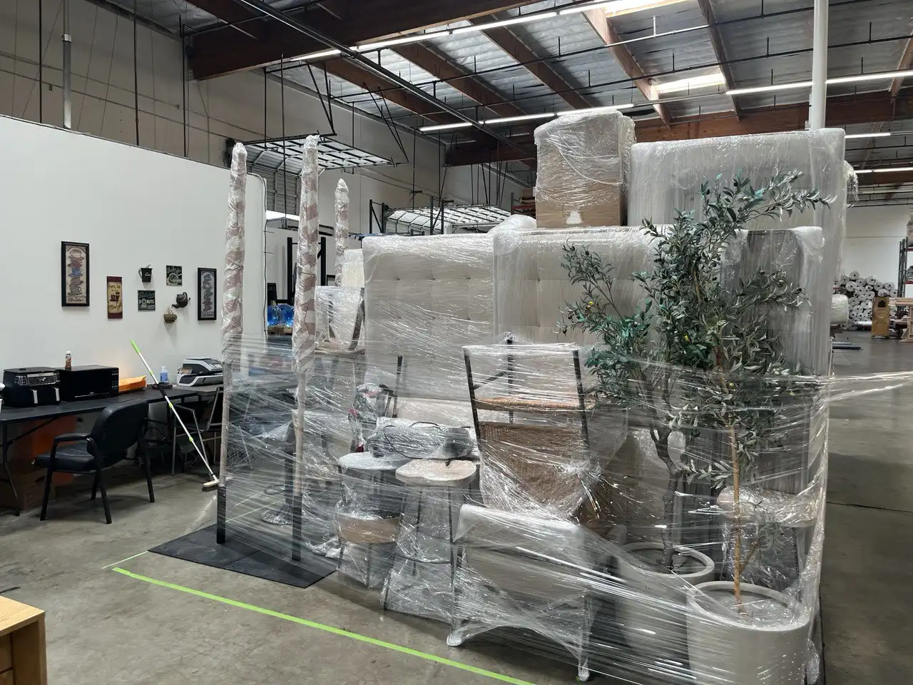 Century City movers carefully wrapping and staging office furniture and decor on pallets inside a warehouse for a commercial relocation