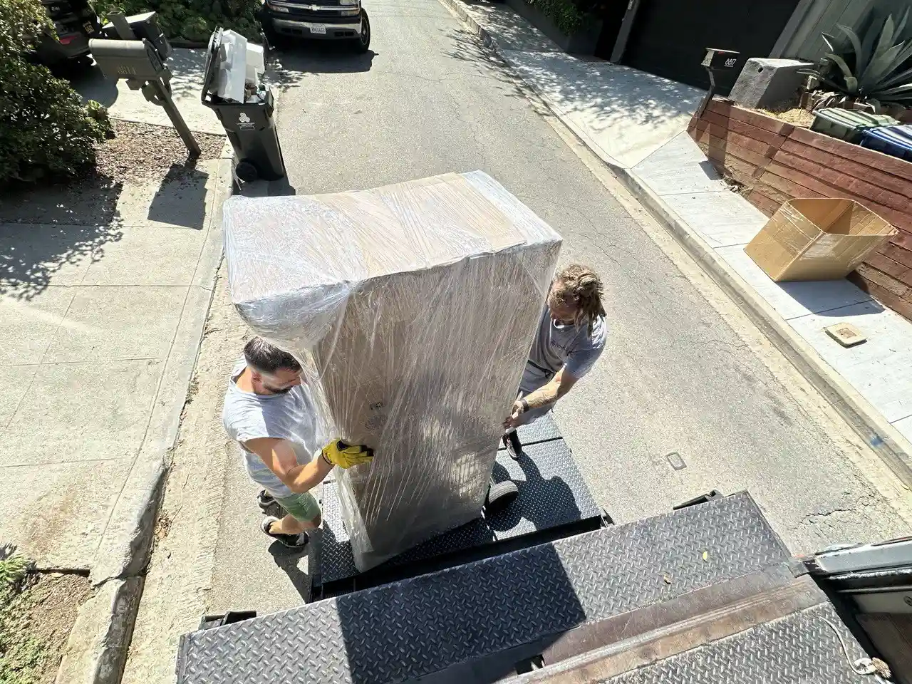 SQ Moving Company crew loading a large wrapped cabinet onto a truck liftgate on a steep residential street in Century City