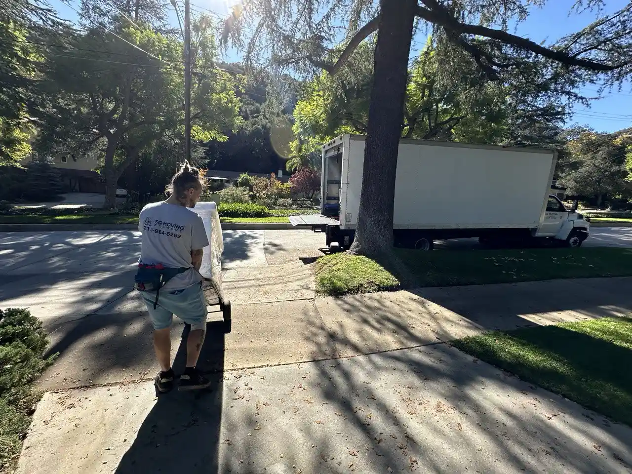SQ Moving Company mover pushing a wrapped cabinet on a dolly toward a box truck on a quiet residential street in Arcadia, CA