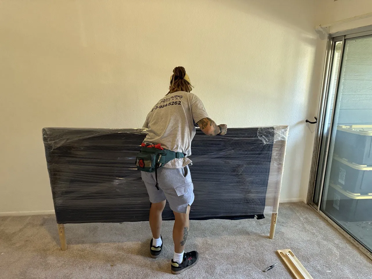 SQ Moving Company mover wrapping a large white dresser with plastic wrap for protection during an indoor move in Arcadia, CA