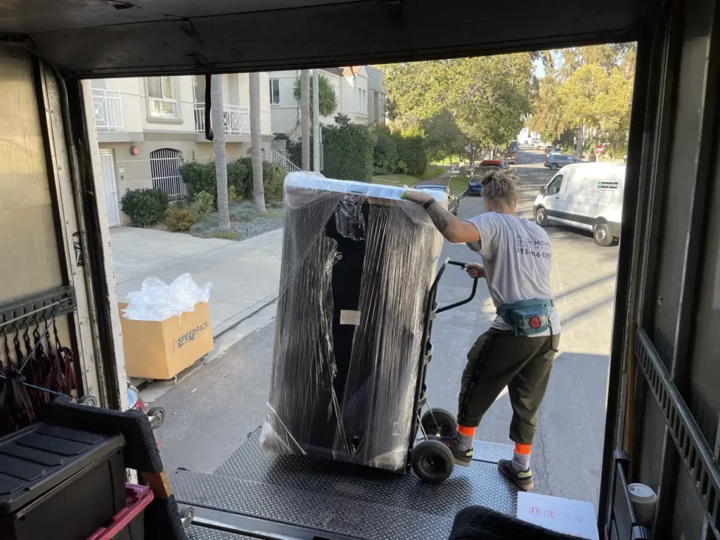 How to Prepare Furniture for Moving in LA: Step-by-Step Guide 11 Moving company in Torrance unloading a shrink-wrapped sofa bed from a moving truck using a hand truck for safe delivery.